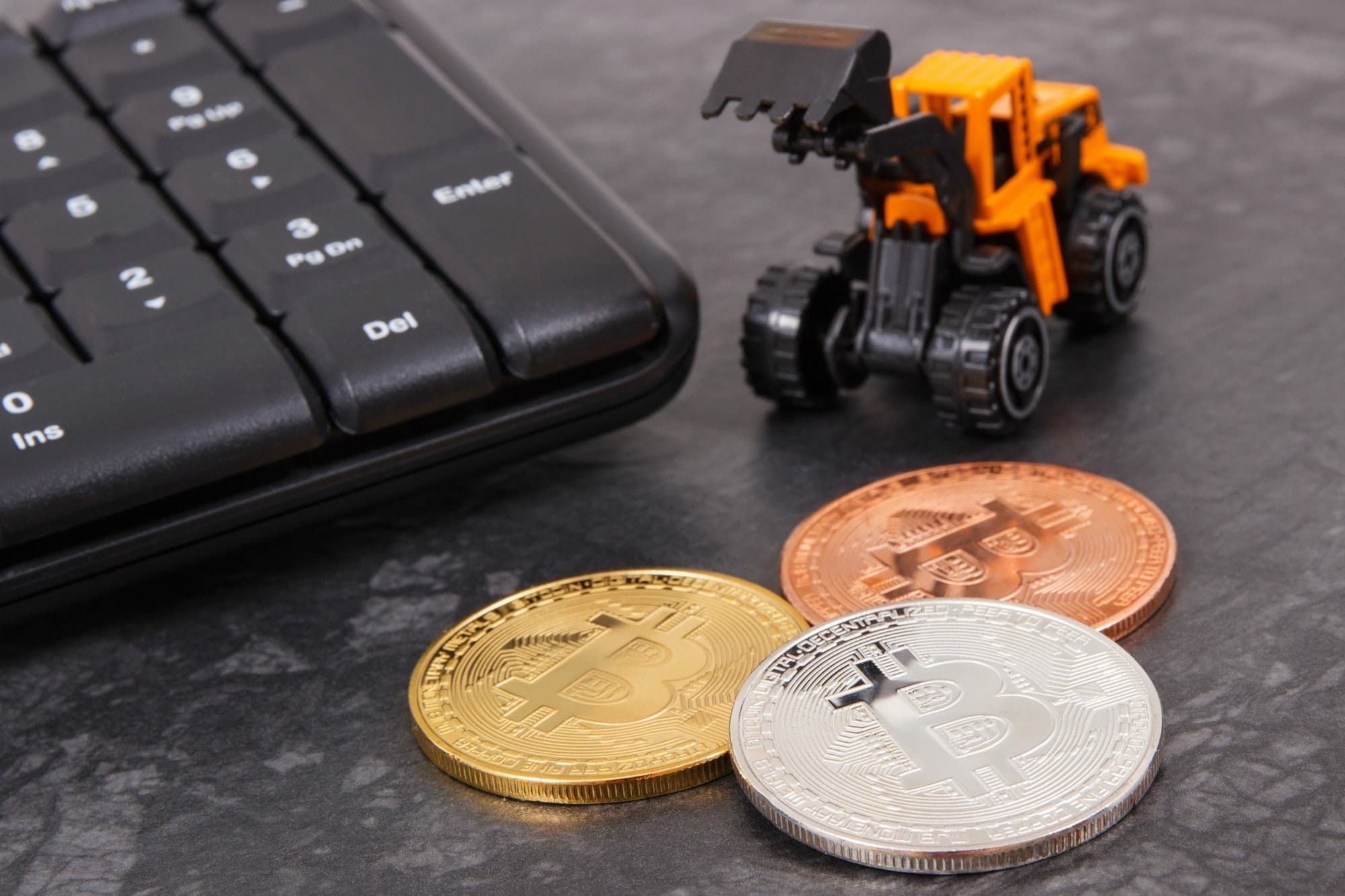 Bitcoins as symbol of electronic virtual money, miniature excavator and computer keyboard