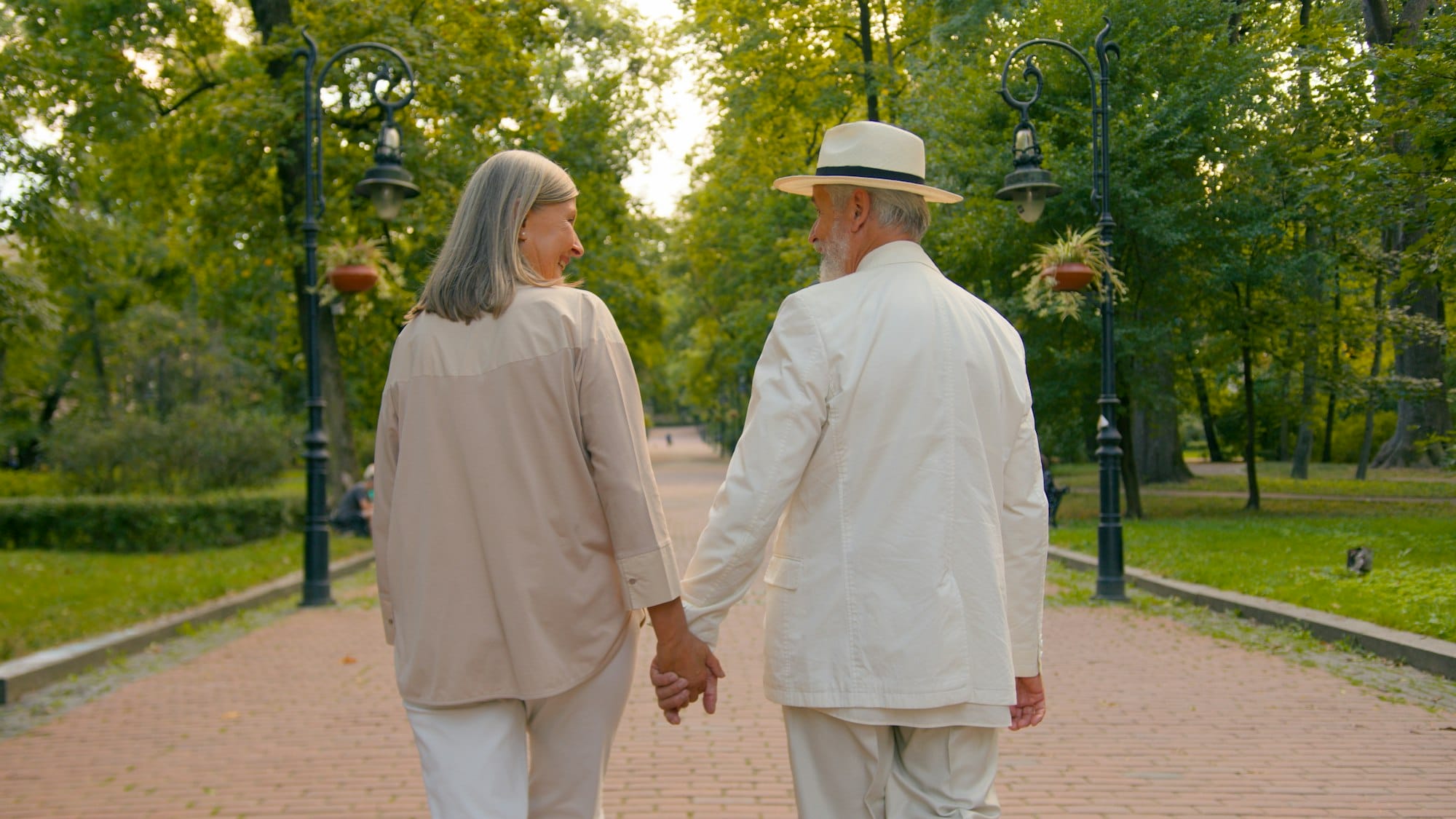 Back view happy Caucasian family old couple man woman holding hands walking together city park